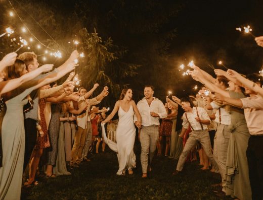 Joyful bride and groom run hand-in-hand through sparkling guests under twinkling night lights